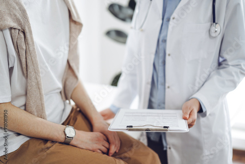 Doctor and patient in clinic. Friendly physician explaining something to young woman while keeping a clipboard with medical records. Medicine concept