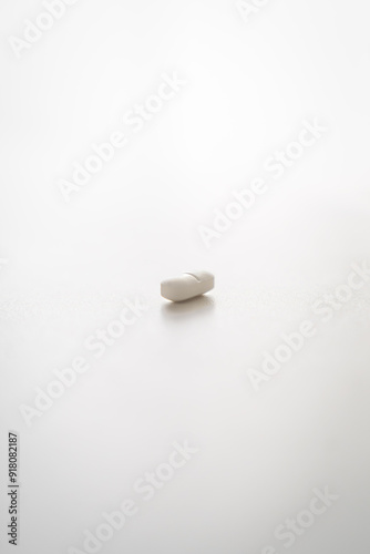 Minimalistic close-up shot of a single white pill isolated on a clean white background with soft shadows.