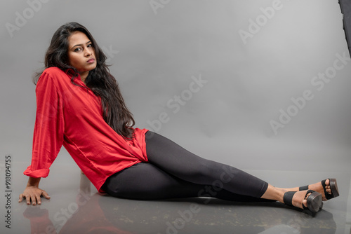 Indian young female model in casual wear posing against grey background - stock photo. Long black haired model wearing red shirt, black jeans and black heeels. photo