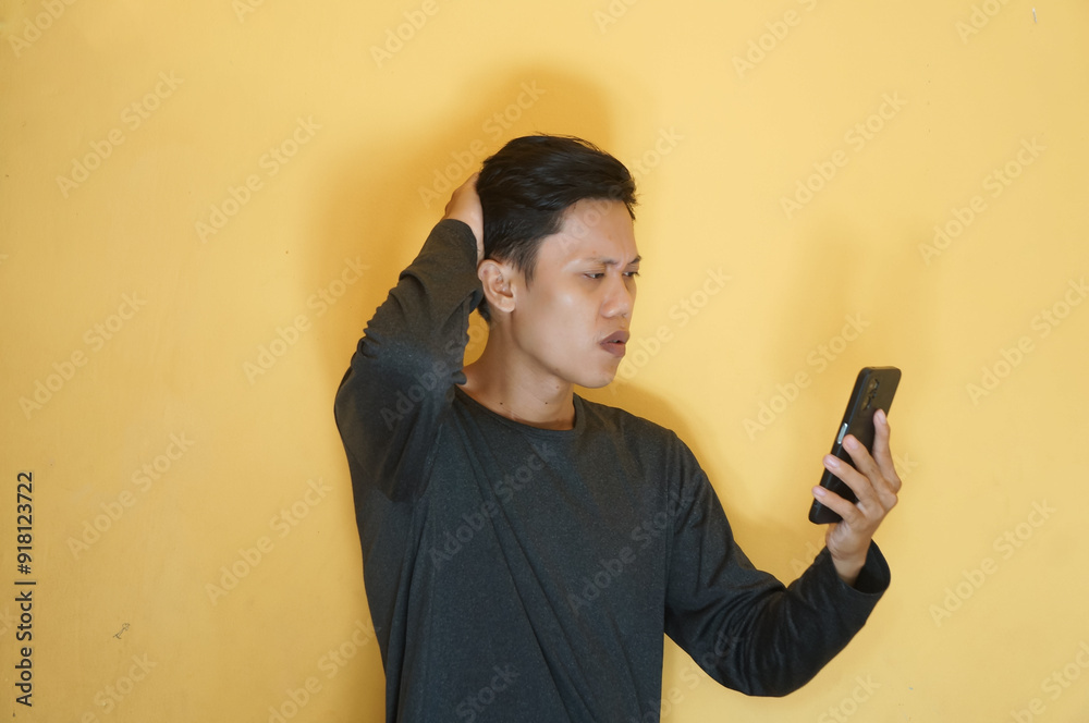 Young Asian man looking at mobile phone with sad expression while holding head Young Asian man looking at mobile phone with sad expression while holding head