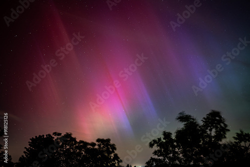 Capture the ethereal beauty of the aurora borealis as it illuminates the warm summer night, casting its colorful glow over the tranquil landscape in Germany.