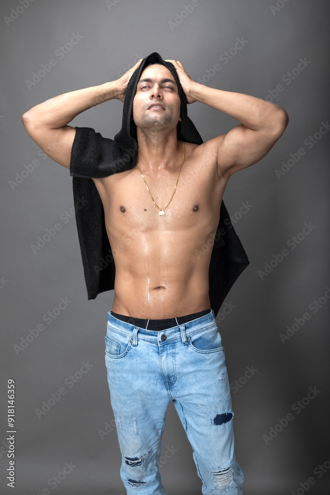 Naklejka premium Cropped view of a young shirtless athlete with black towel after shower, bath or sauna. Indian bodybuilder with happy, mischievous facial expressions posing for camera