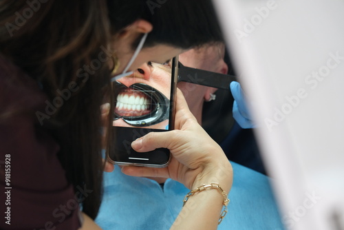 Dentist performing dental surgery and person taking photo of dental treatment with phone