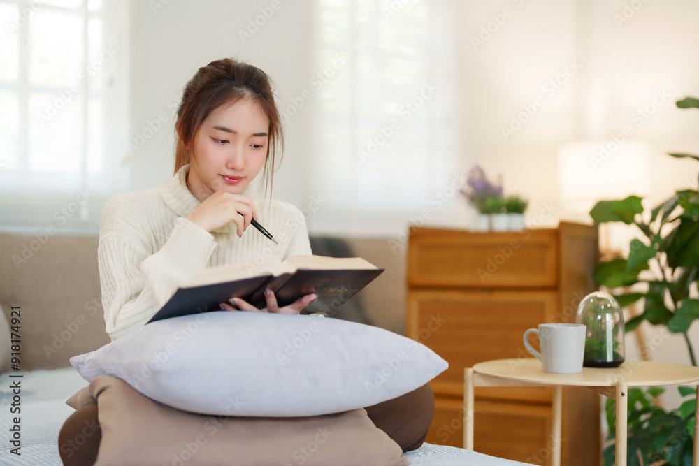 Young asian women in sweater sitting on comfortable couch and reading a book for thinking and learning education while relaxation and doing activity to spending time with slow life lifestyle at home Young asian women in sweater sitting on comfortable couch and reading a book for thinking and learning education while relaxation and doing activity to spending time with slow life lifestyle at home
