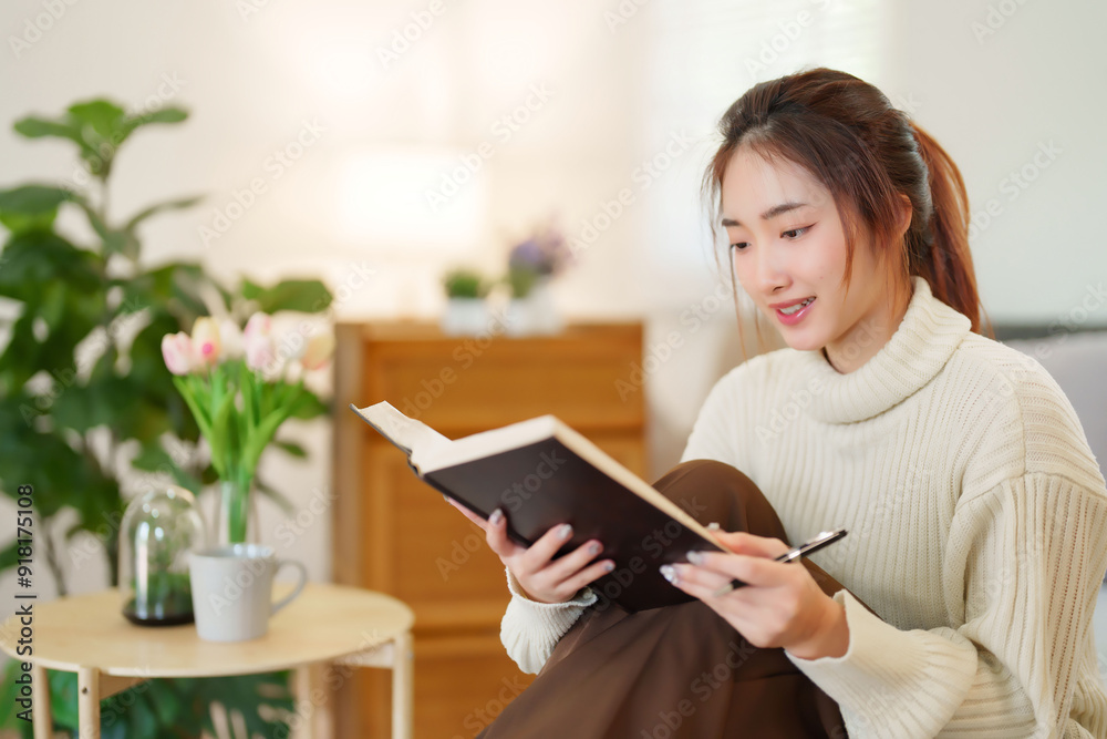 Young asian women in sweater reading the book to learning about knowledge and education while sitting on couch to relaxation and doing activity for spending time with slow life lifestyle at home Young asian women in sweater reading the book to learning about knowledge and education while sitting on couch to relaxation and doing activity for spending time with slow life lifestyle at home