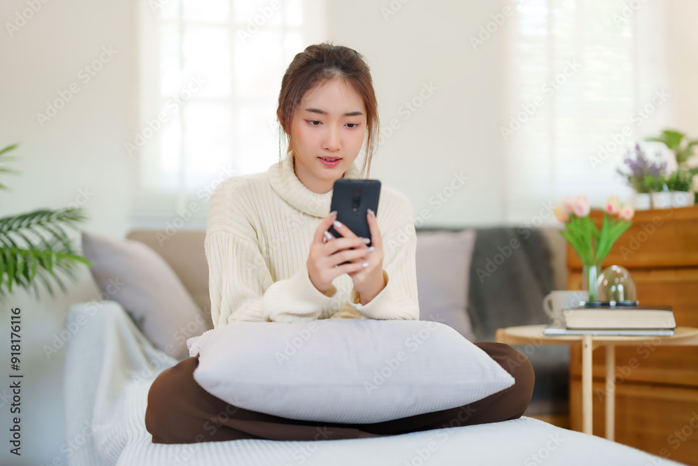 Young asian women in sweater enjoying with surfing entertainment on smartphone while sitting on comfortable couch to relaxation and doing activity for spending time with slow life lifestyle at home Young asian women in sweater enjoying with surfing entertainment on smartphone while sitting on comfortable couch to relaxation and doing activity for spending time with slow life lifestyle at home