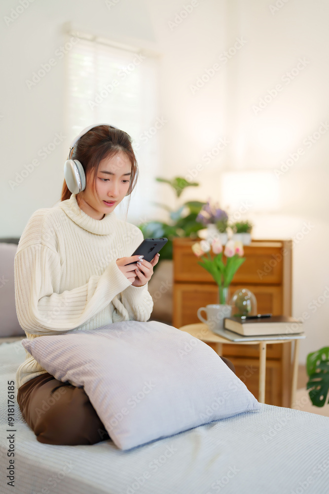 Young asian women in sweater wearing headphone and surfing entertainment with listening music on smartphone while relaxation and doing activity for spending time with slow life lifestyle at home Young asian women in sweater wearing headphone and surfing entertainment with listening music on smartphone while relaxation and doing activity for spending time with slow life lifestyle at home