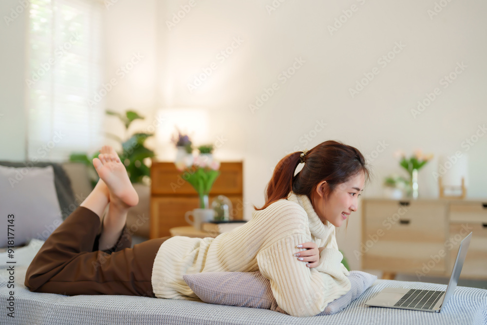 Young asian women in sweater lying on the couch to enjoying with watching social media entertainment on laptop while relaxation and doing activity to spending time with slow life lifestyle at home Young asian women in sweater lying on the couch to enjoying with watching social media entertainment on laptop while relaxation and doing activity to spending time with slow life lifestyle at home