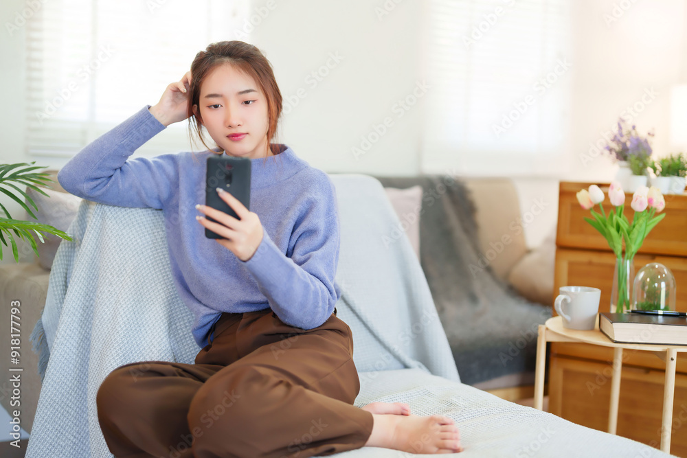 Young asian women in sweater using smartphone to chatting on social media and entertainment while sitting on sofa to relaxation and doing activity for spending time with slow life lifestyle at home Young asian women in sweater using smartphone to chatting on social media and entertainment while sitting on sofa to relaxation and doing activity for spending time with slow life lifestyle at home