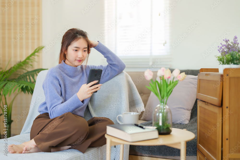 Young asian women in sweater using smartphone to watching on social media and entertainment while sitting on couch to relaxation and doing activity for spending time with slow life lifestyle at home Young asian women in sweater using smartphone to watching on social media and entertainment while sitting on couch to relaxation and doing activity for spending time with slow life lifestyle at home