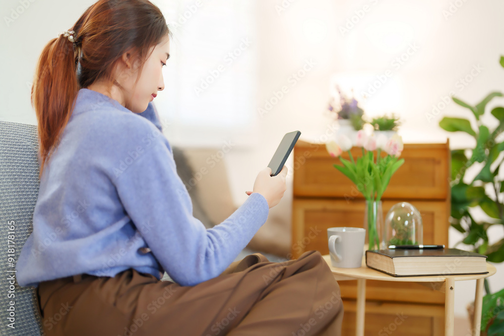 Young asian women in sweater using smartphone to surfing on social media and entertainment while sitting on couch to relaxation and doing activity for spending time with slow life lifestyle at home Young asian women in sweater using smartphone to surfing on social media and entertainment while sitting on couch to relaxation and doing activity for spending time with slow life lifestyle at home