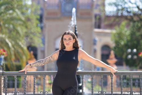 Konstfotografi young and beautiful brunette latin woman dressed in a black lycra jumpsuit leaning on the wrought iron railing