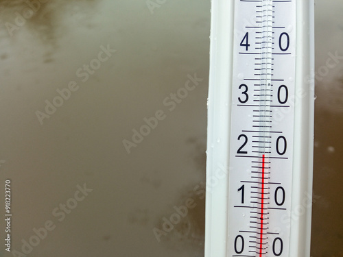 A thermometer on the background of a puddle. Autumn weather. The thermometer is 20 degrees. Cold snap. Rains, downpours. photo