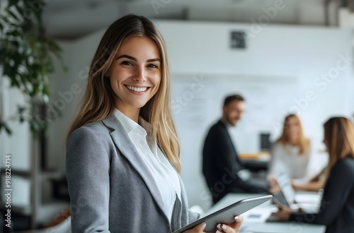 A smiling businesswoman stands in an office holding her tablet