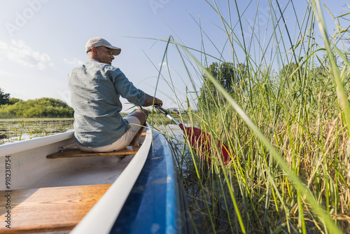 Young man having an active vacation on a beautiful lakeshore, paddling a canoe and enjoying the green landscape. photo