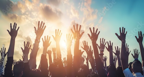 Silhouettes of a crowd of people raising their hands in the air against a bright sunset sky.