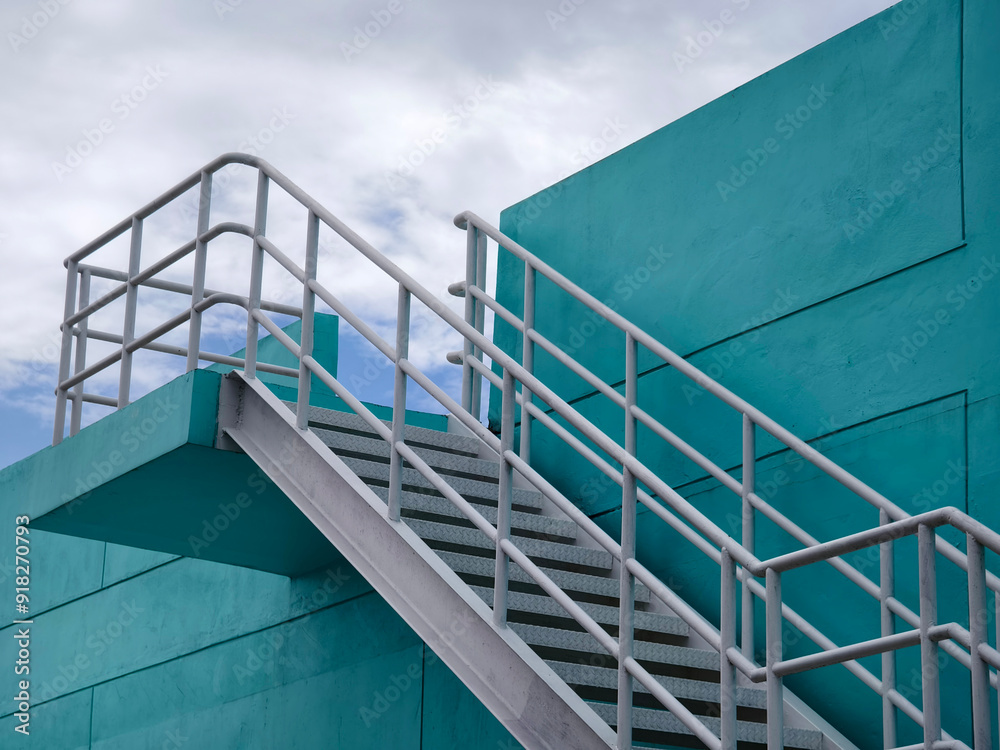 Metal stairs to blue building against sky and clouds Metal stairs to blue building against sky and clouds