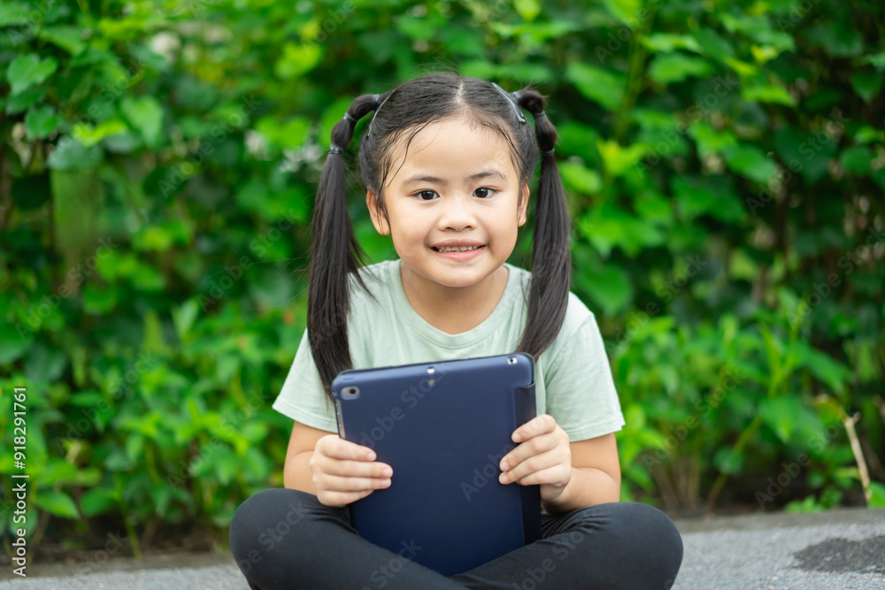 Asian little child girl playing tablet and smartphone happiness. child girl relaxing at the Park. Play tablet and smartphone concept. Asian little child girl playing tablet and smartphone happiness. child girl relaxing at the Park. Play tablet and smartphone concept.