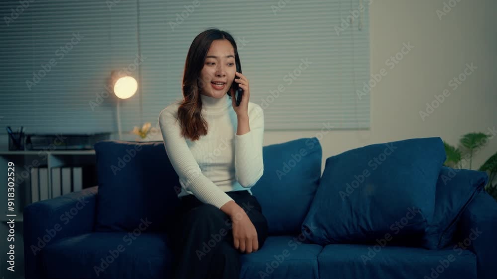 Young woman talking on phone while sitting on stylish blue sofa in cozy living room with modern decor and soft lighting Young woman talking on phone while sitting on stylish blue sofa in cozy living room with modern decor and soft lighting