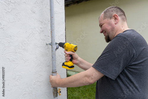 A dedicated individual expertly secures a pipe fitting to a white wall, showcasing craftsmanship on a sunny day in a residential setting. photo