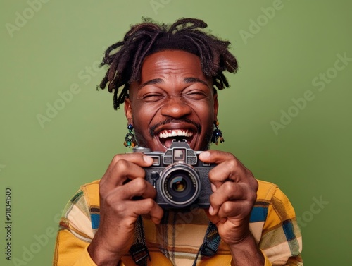 Photo of overjoyed man with stylish earrings dressed in a trendy top holding a camera in hands grinning isolated on olive green color background