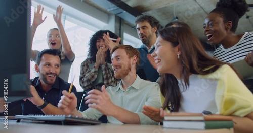 Multi-ethnic group of people at work. Looking patiently at screen. Waiting for important moment. After seeing positive result everyone exclaiming. Clapping their hands while smiling with joy.