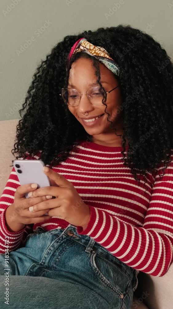Smiling woman sitting on sofa in living room texting sms using mobile phone Smiling woman sitting on sofa in living room texting sms using mobile phone