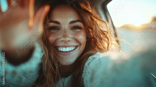 A joyous woman with curly hair is captured smiling and waving while bathed in sunshine. Her radiant happiness and warmth are evident, creating a lively, uplifting image. photo