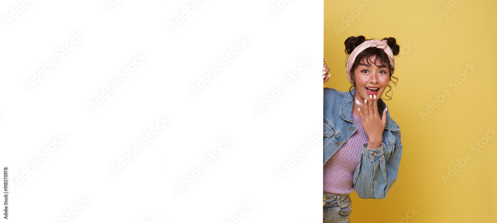 Φωτογραφία Cheerful Young Asian teen woman is standing behind the white blank banner or empty copy space advertisement board on yellow background