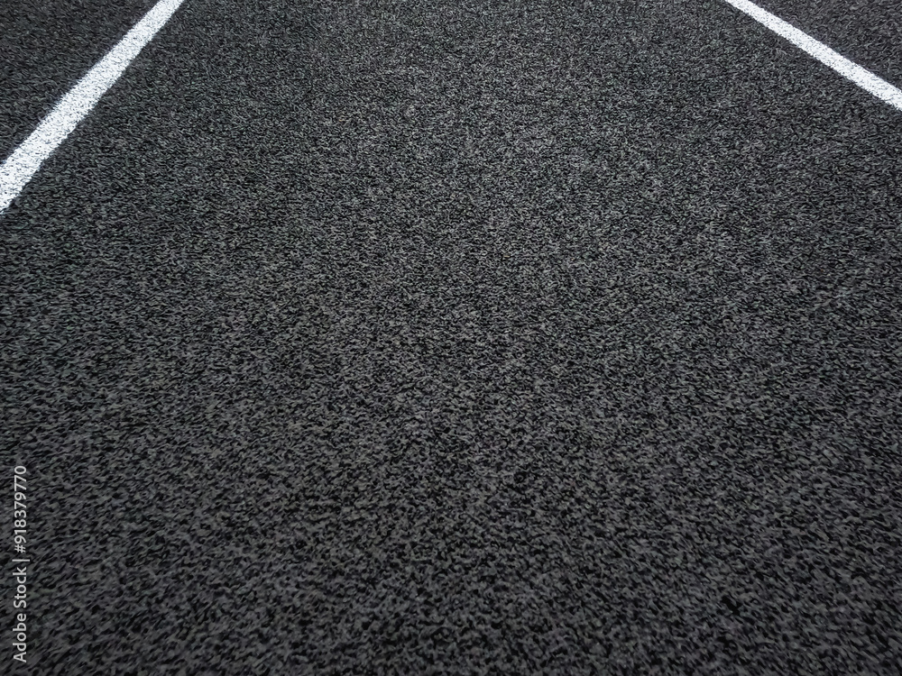 Fototapeta premium Rubber black running track surface with white lane lines. Surface level view of the textured artificial black surface.
