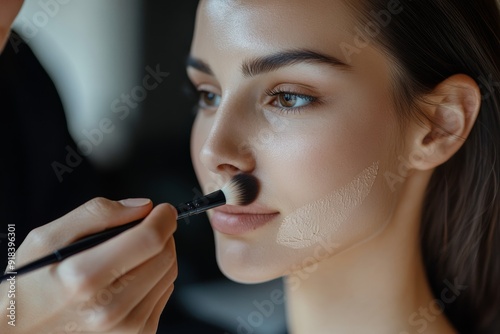 A makeup artist focuses on applying foundation to a model's face, showcasing precision and artistry in a professional studio environment