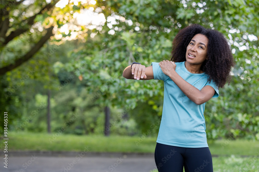 African American female athlete outdoors in a park experiencing shoulder pain while working out. Injury during fitness training session, highlighting challenges athletes encounter. Activewear fashion African American female athlete outdoors in a park experiencing shoulder pain while working out. Injury during fitness training session, highlighting challenges athletes encounter. Activewear fashion