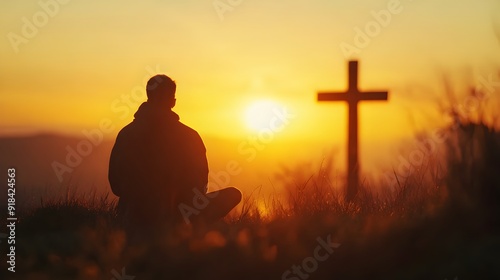 Silhouette of a man sitting in front of a cross at sunset