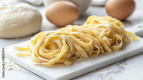 Floured fresh noodles artfully arranged on a white marble board, with eggs and dough in the background, ready to be cooked for a delicious meal.