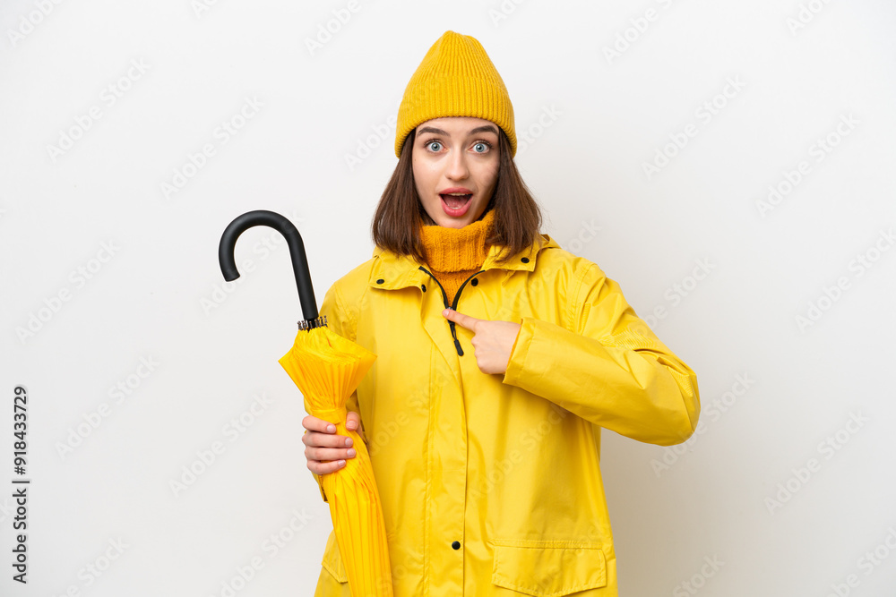Young Ukrainian woman with rainproof coat and umbrella isolated on white background with surprise facial expression Young Ukrainian woman with rainproof coat and umbrella isolated on white background with surprise facial expression