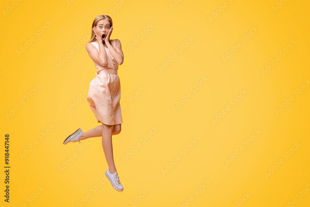 Fototapeta premium Shocking Sale. Young Woman Jumping In Air And Touching Face With Amazement, Shouting Wow With Open Mouth, Posing Over Yellow Background