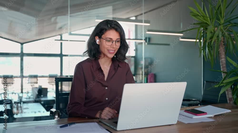 Middle easter business woman in earphones having virtual team meeting video conference call. Latin businesswoman using laptop talking to coworkers, partners in remote online chat, sitting in office