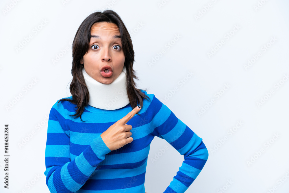 Young hispanic woman wearing neck brace isolated on white background surprised and pointing side Young hispanic woman wearing neck brace isolated on white background surprised and pointing side