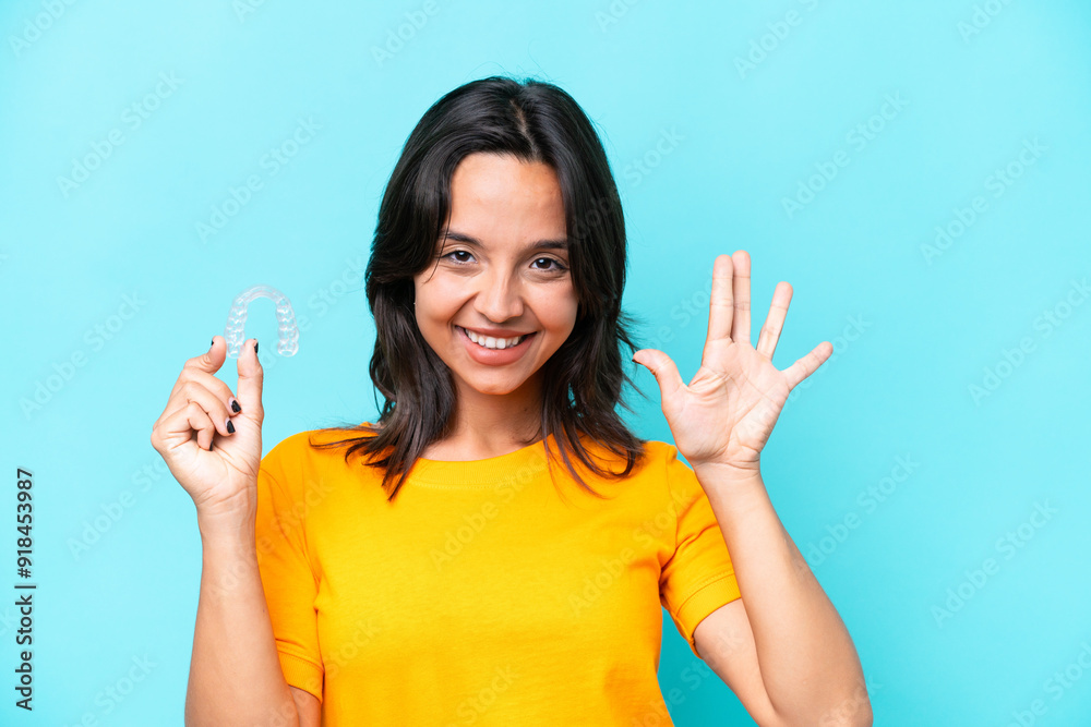 Young hispanic woman holding invisible braces isolated on blue background counting five with fingers Young hispanic woman holding invisible braces isolated on blue background counting five with fingers