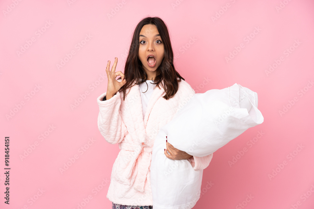 Young woman in pajamas isolated on pink background surprised and showing ok sign Young woman in pajamas isolated on pink background surprised and showing ok sign