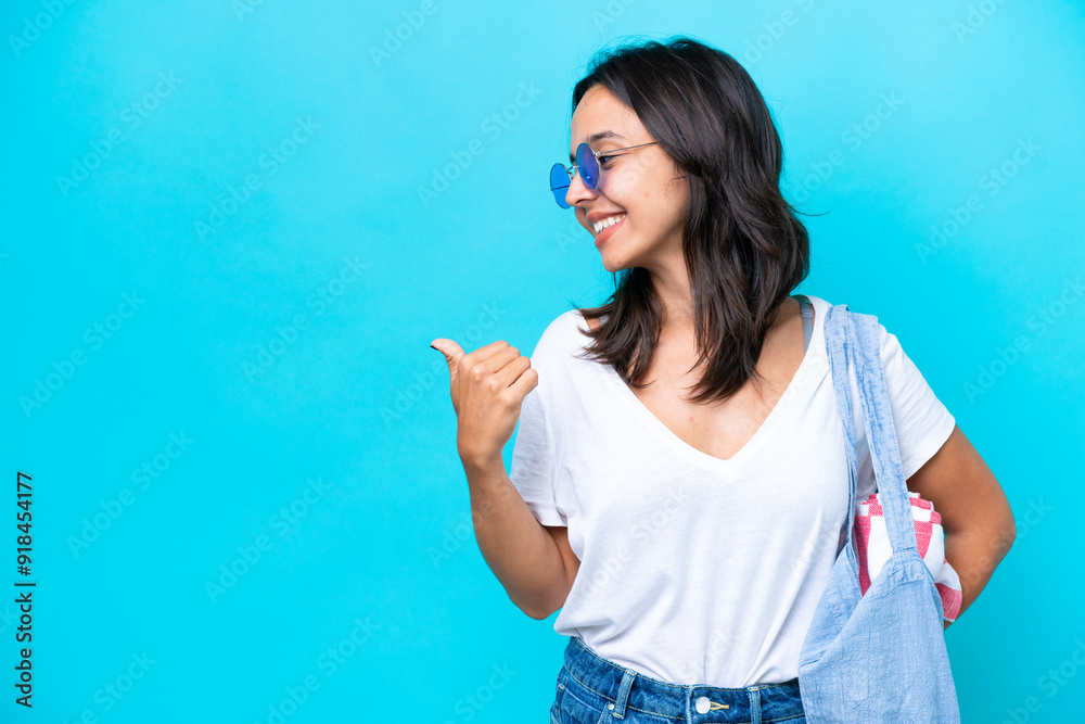 Young caucasian woman holding a beach bag isolated on blue background pointing to the side to present a product Young caucasian woman holding a beach bag isolated on blue background pointing to the side to present a product
