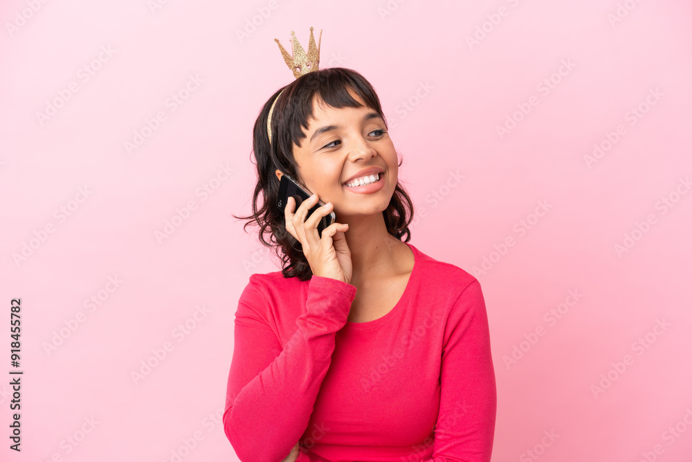 Young mixed race princess with crown isolated on pink background keeping a conversation with the mobile phone Young mixed race princess with crown isolated on pink background keeping a conversation with the mobile phone