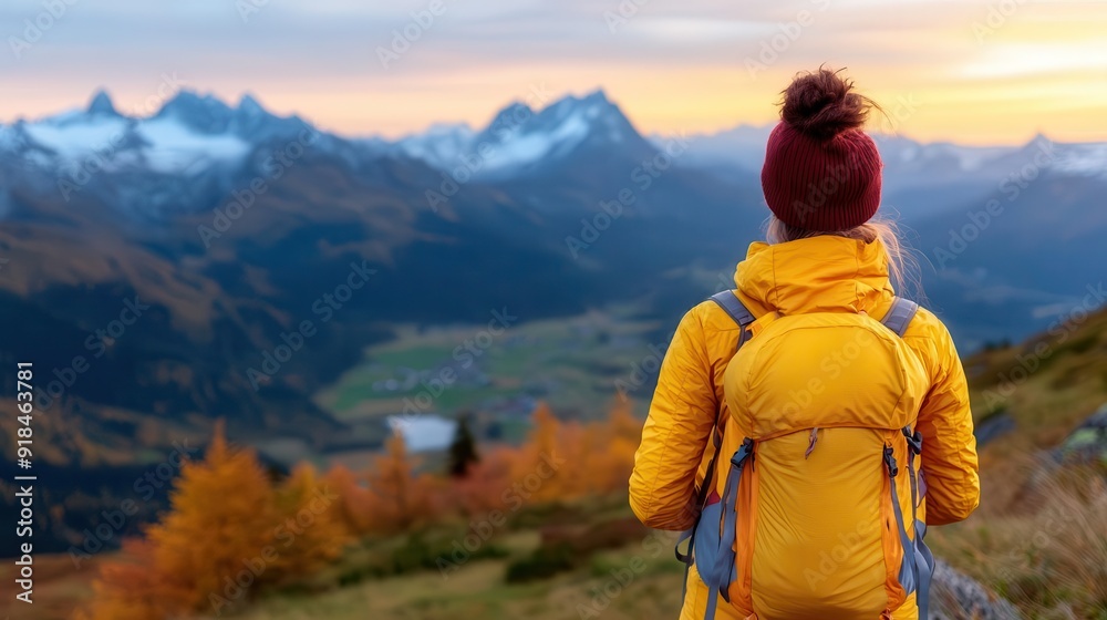 A traveler in a bright yellow jacket enjoys a stunning mountain sunset, surrounded by beautiful autumn scenery and majestic peaks. A traveler in a bright yellow jacket enjoys a stunning mountain sunset, surrounded by beautiful autumn scenery and majestic peaks.