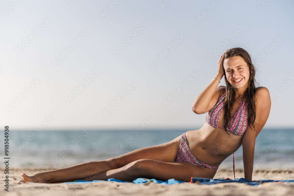 Smiling woman in bikini relaxing on sunny beach with serene ocean background Smiling woman in bikini relaxing on sunny beach with serene ocean background