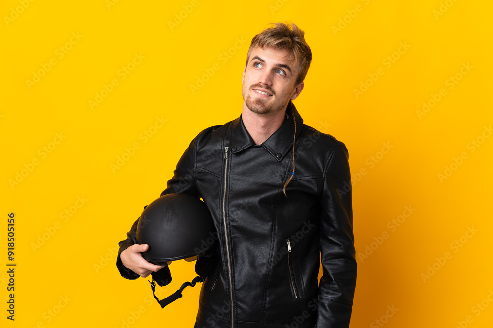 Man with a motorcycle helmet isolated on yellow background thinking an idea while looking up Man with a motorcycle helmet isolated on yellow background thinking an idea while looking up