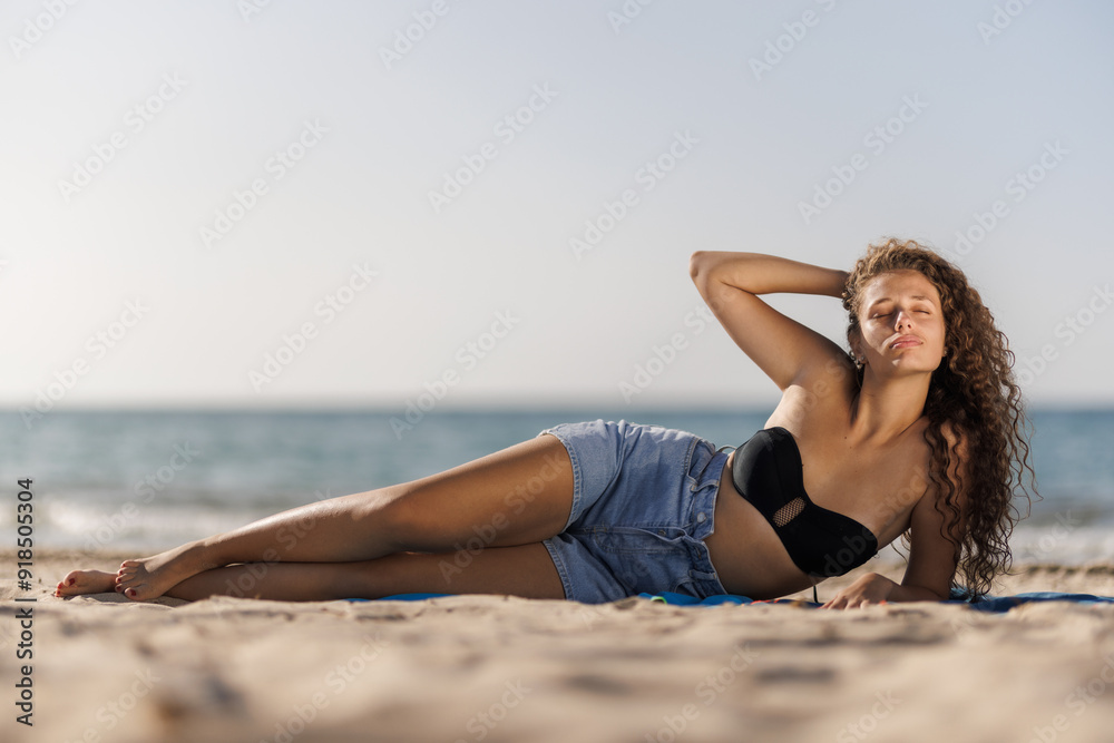 Relaxed woman sunbathing on sandy beach in summer, enjoying sunny day by the sea Relaxed woman sunbathing on sandy beach in summer, enjoying sunny day by the sea