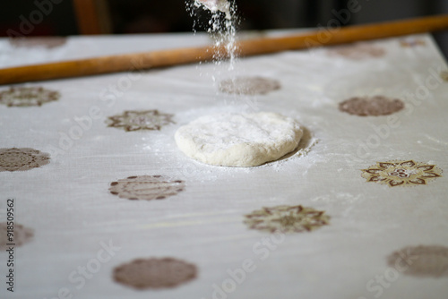 Old woman hand pouring flour on a raw dough before rolling it with a rolling pin photo