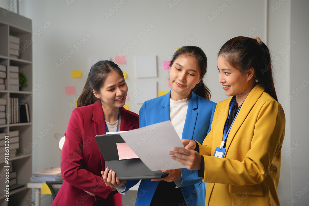 Three young businesswomen smiling and working together using a digital tablet and analyzing documents in the office Three young businesswomen smiling and working together using a digital tablet and analyzing documents in the office