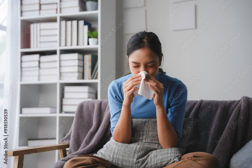 Young asian woman is sitting on her couch at home, blowing her nose with a tissue Young asian woman is sitting on her couch at home, blowing her nose with a tissue