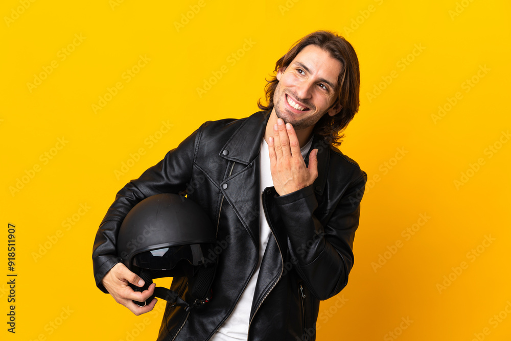 Man with a motorcycle helmet isolated on yellow background looking up while smiling Man with a motorcycle helmet isolated on yellow background looking up while smiling